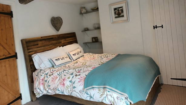 A bedroom with a wooden headboard, floral bedding, a teal throw blanket, a heart-shaped decoration, and a white wardrobe with black handles. - Beautiful 2 bedroom spacious Cottage in the heart of historic Richmond  (Richmond)
