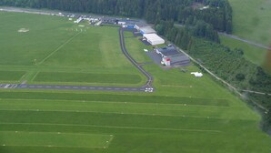 An aerial view of a rural airport with a runway, hangars, and surrounding fields.