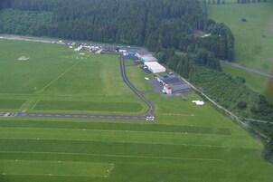 Vista aérea de um aeroporto rural com pista, hangares e campos ao redor.