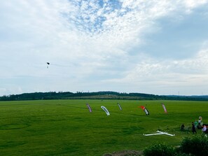 Un vaste champ herbeux, dégagé de tout obstacle, où plusieurs cerfs-volants s’élèvent dans les airs.