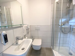 Une salle de bain moderne avec une douche à l’italienne en verre, un lavabo blanc et des toilettes.