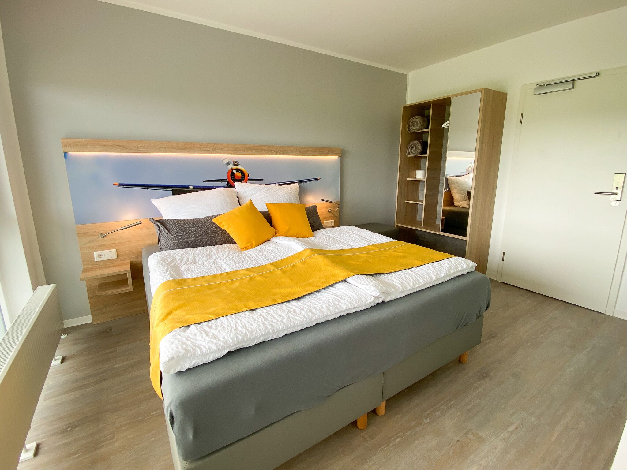 Une chambre à coucher moderne avec un lit, une tête de lit dotée d’un luminaire, une table de chevet en bois et une armoire.