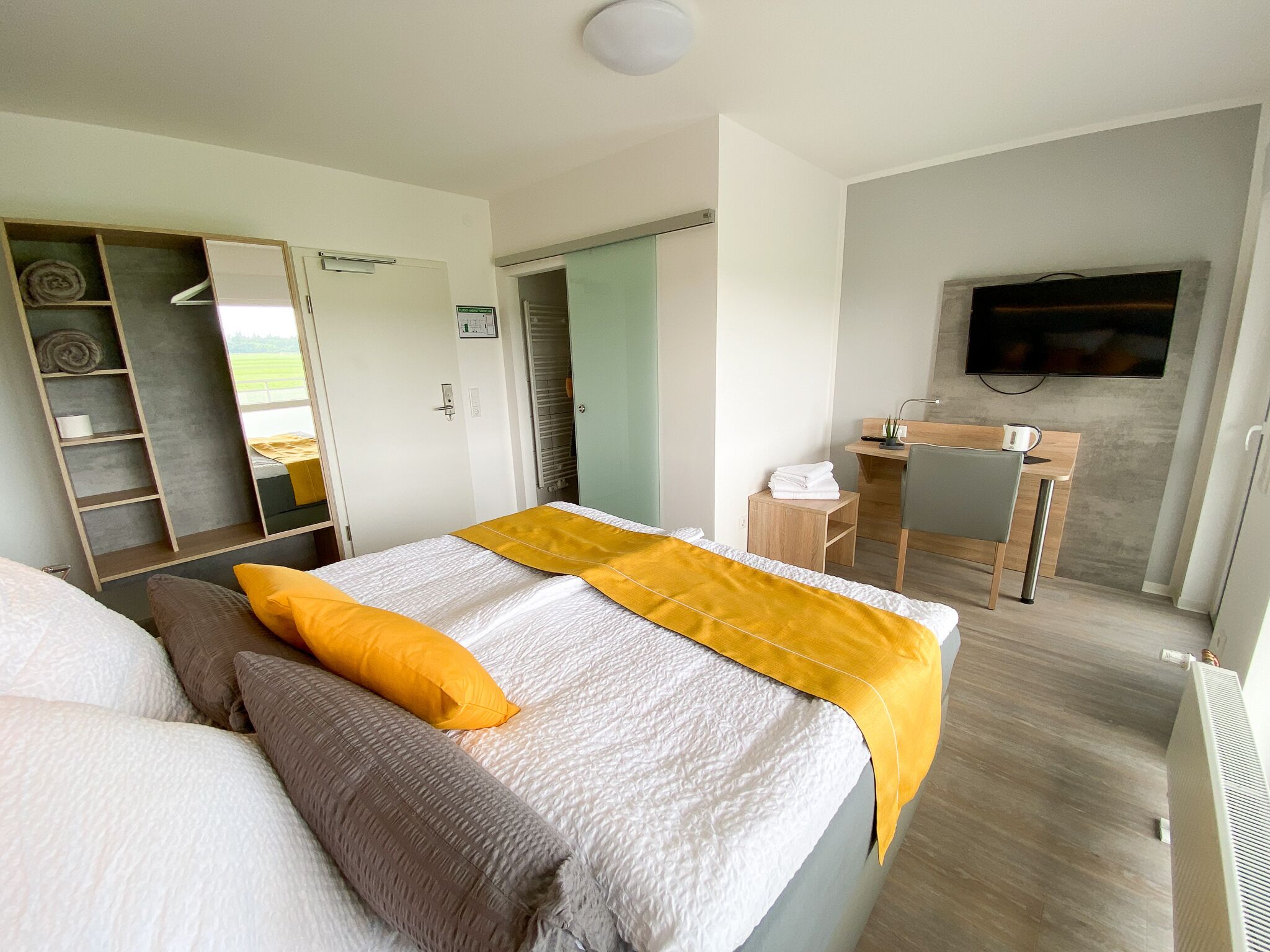 A modern bedroom with a bed, a desk, a TV, and a walk-in closet.