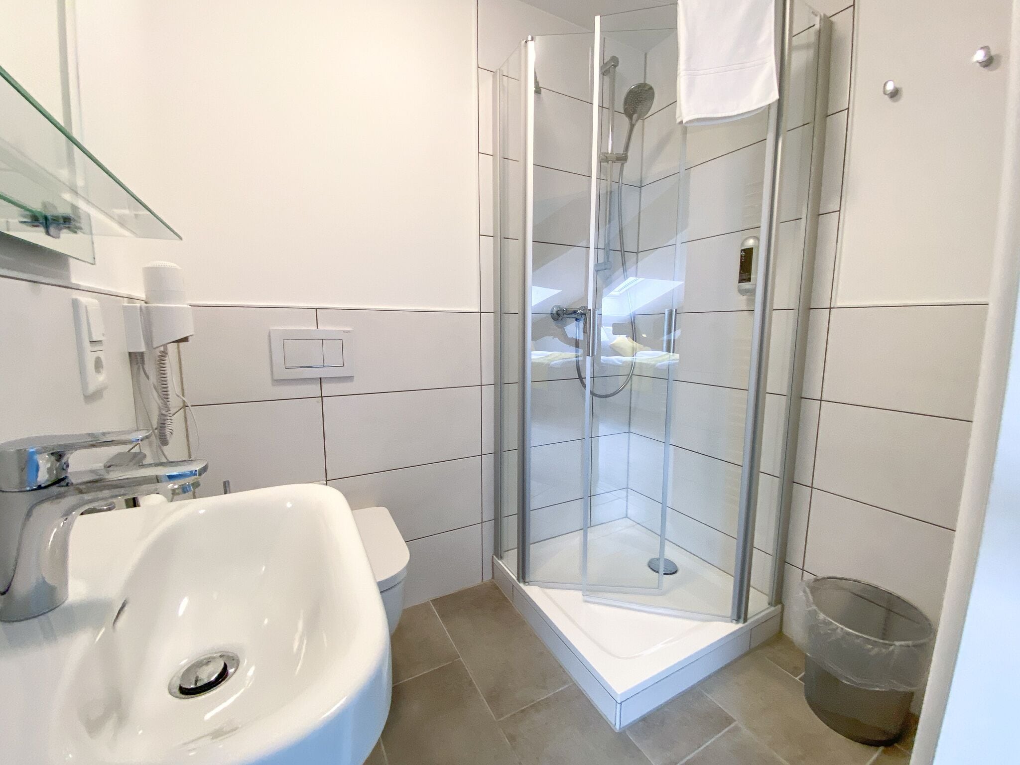 A modern bathroom with a glass-enclosed shower, a white sink, and a trash bin.