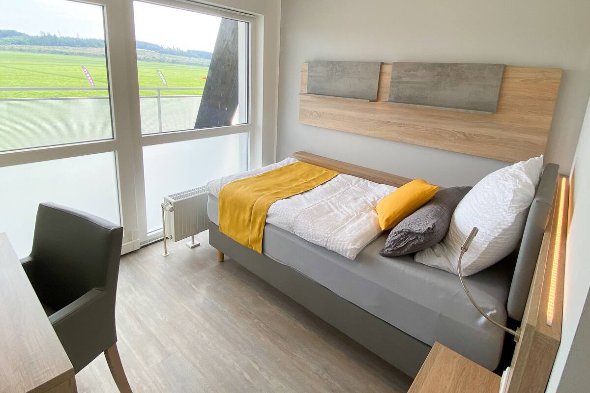 Une chambre moderne avec une grande fenêtre, un lit doté d’une tête de lit en bois et un radiateur.