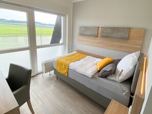 Une chambre moderne avec une grande fenêtre, un lit doté d’une tête de lit en bois et un radiateur.