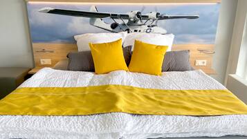 Ein Bett mit einer weißen und gelben Tagesdecke, zwei gelben Kissen und einem Kopfteil mit einem Bild eines Militärflugzeugs.