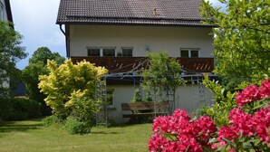 Ein Haus mit einem Ziegeldach, einer Holzterrasse und einem Garten mit blühenden Pflanzen.