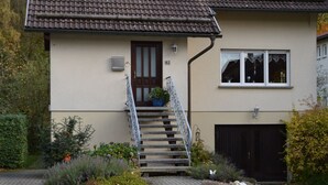 Ein zweistöckiges Haus mit Eingangsbereich, Treppe, Garage und einem Garten mit verschiedenen Pflanzen.