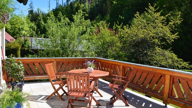 Eine Holzterrasse mit rundem Tisch und Stühlen, umgeben von einer Holzbrüstung.