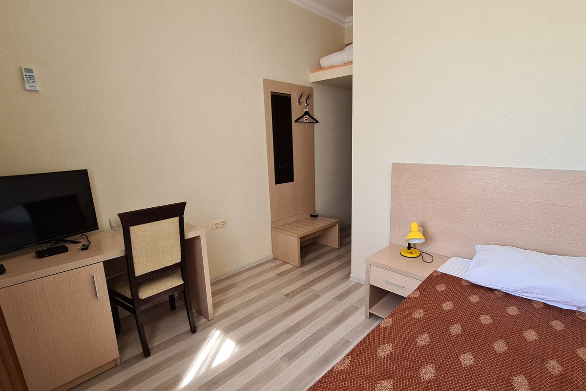 Une chambre d’hôtel comprenant un lit, une table de chevet avec une lampe, un téléviseur, un bureau avec une chaise et une armoire.