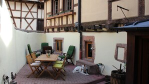 Un patio con una mesa y sillas de madera, un perro y un edificio rústico con techo de tejas.