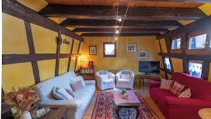 Una sala de estar con un sofá blanco, un sofá rojo, dos sillones blancos, una mesa de centro de madera y una alfombra estampada.