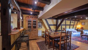 Un comedor con mesa y sillas de madera, una cocina con un armario, y una sala de estar con sofá y lámpara.