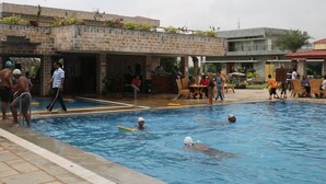 Zona de piscina con edificio de piedra, mobiliario exterior y un área cubierta.
