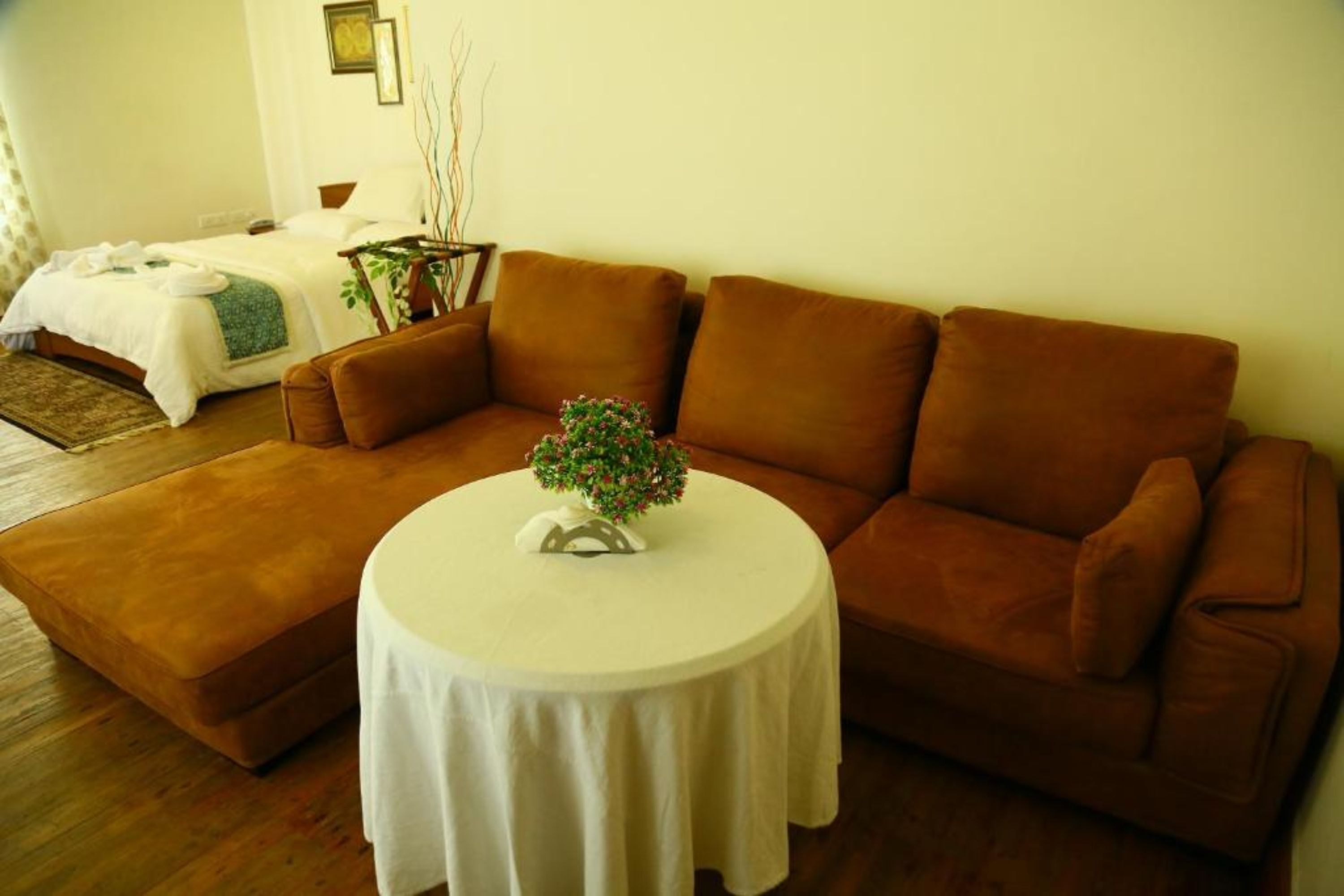 A living room with a brown sofa, a round coffee table, and a bed with a white bedspread in the background.