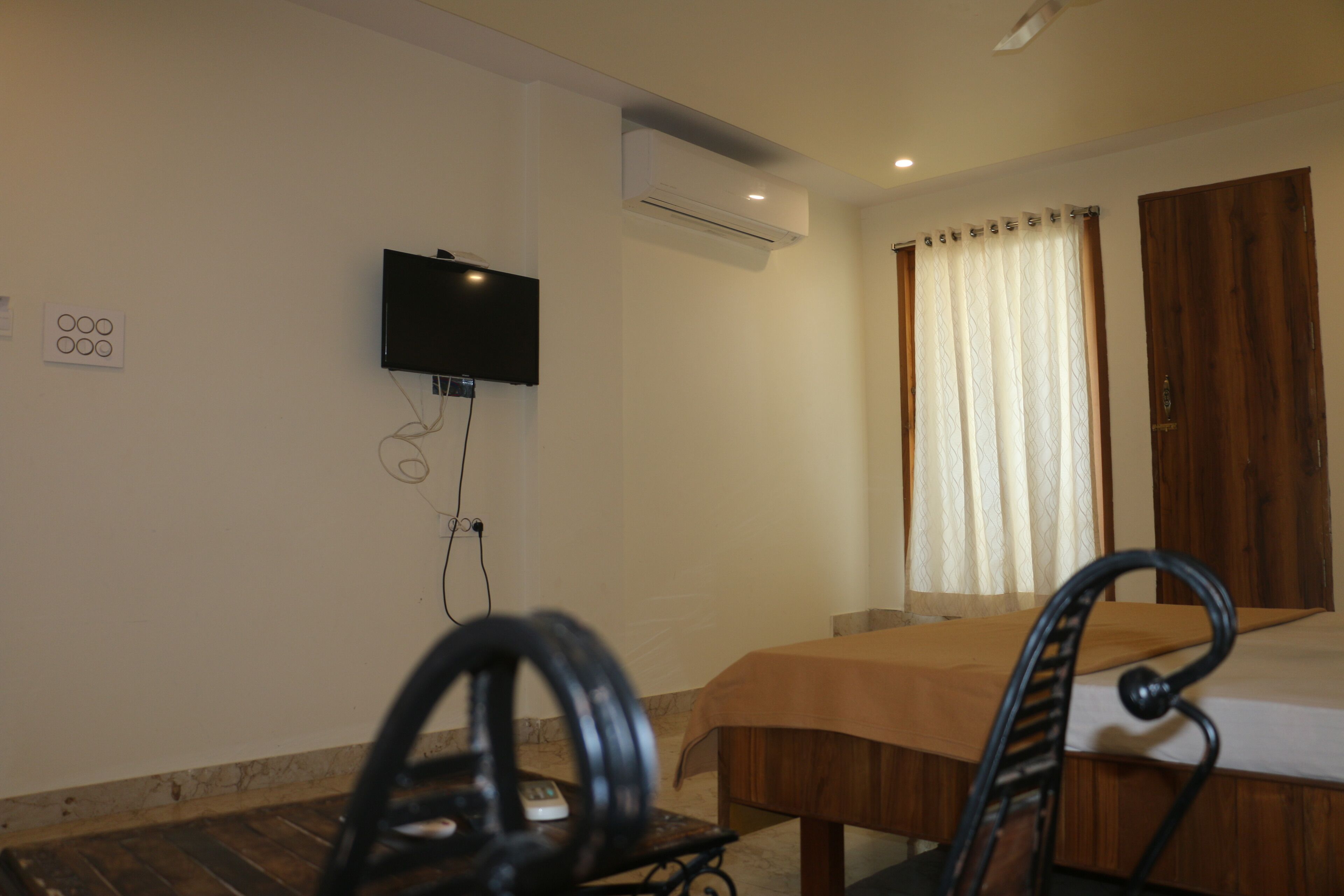 Habitación de hotel con cama, televisión montada en la pared, aire acondicionado, puerta de madera y cortina.