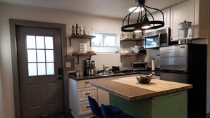 Ett kök med en köksö i trä, barstolar, ett kylskåp, en mikrovågsugn och en kaffebryggare.