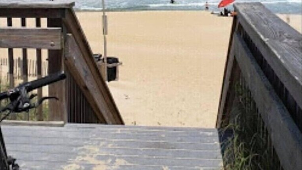 Een houten looppad naar een zandstrand, met de oceaan op de achtergrond.