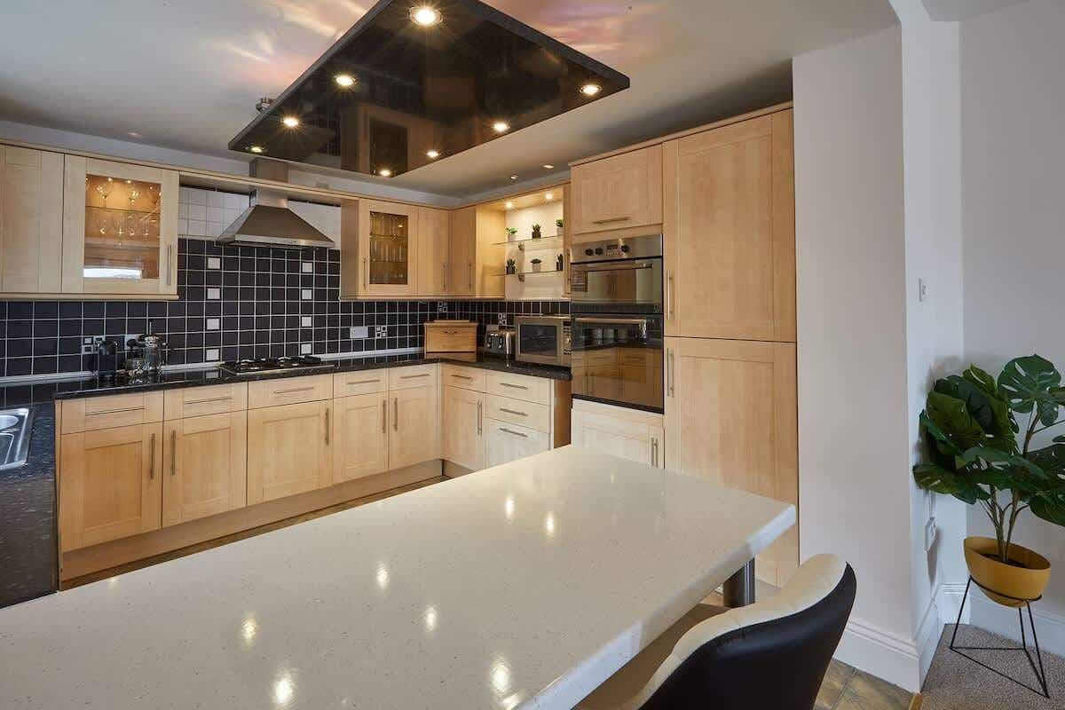 Une cuisine moderne avec des meubles en bois, un dosseret en carreaux noirs et des appareils électroménagers en acier inoxydable.