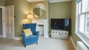 A living room with a blue armchair, a round mirror, a fireplace, and a television. - Host & Stay | Henderson House (Whitby)