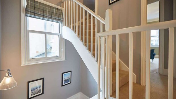 A staircase with white railings leading to an upper floor, a window with blinds, and framed pictures on the wall. - Host & Stay | Henderson House (Whitby)