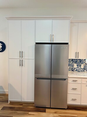 Eine Küche mit einem Edelstahl-Kühlschrank mit zwei Türen, weißen Schränken und einer blauen Mosaik-Spritzwand.