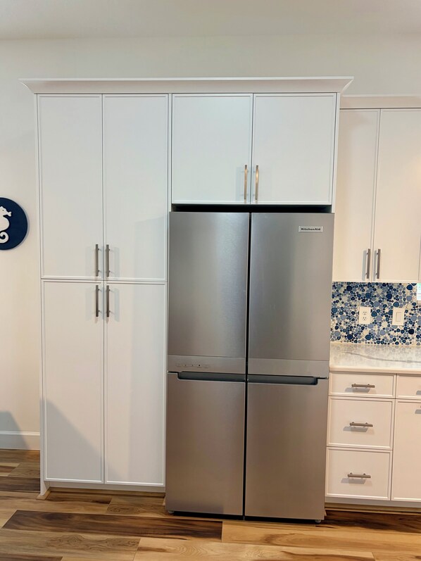 Cozinha com geladeira de porta dupla em aço inoxidável, armários brancos e backsplash de mosaico azul.
