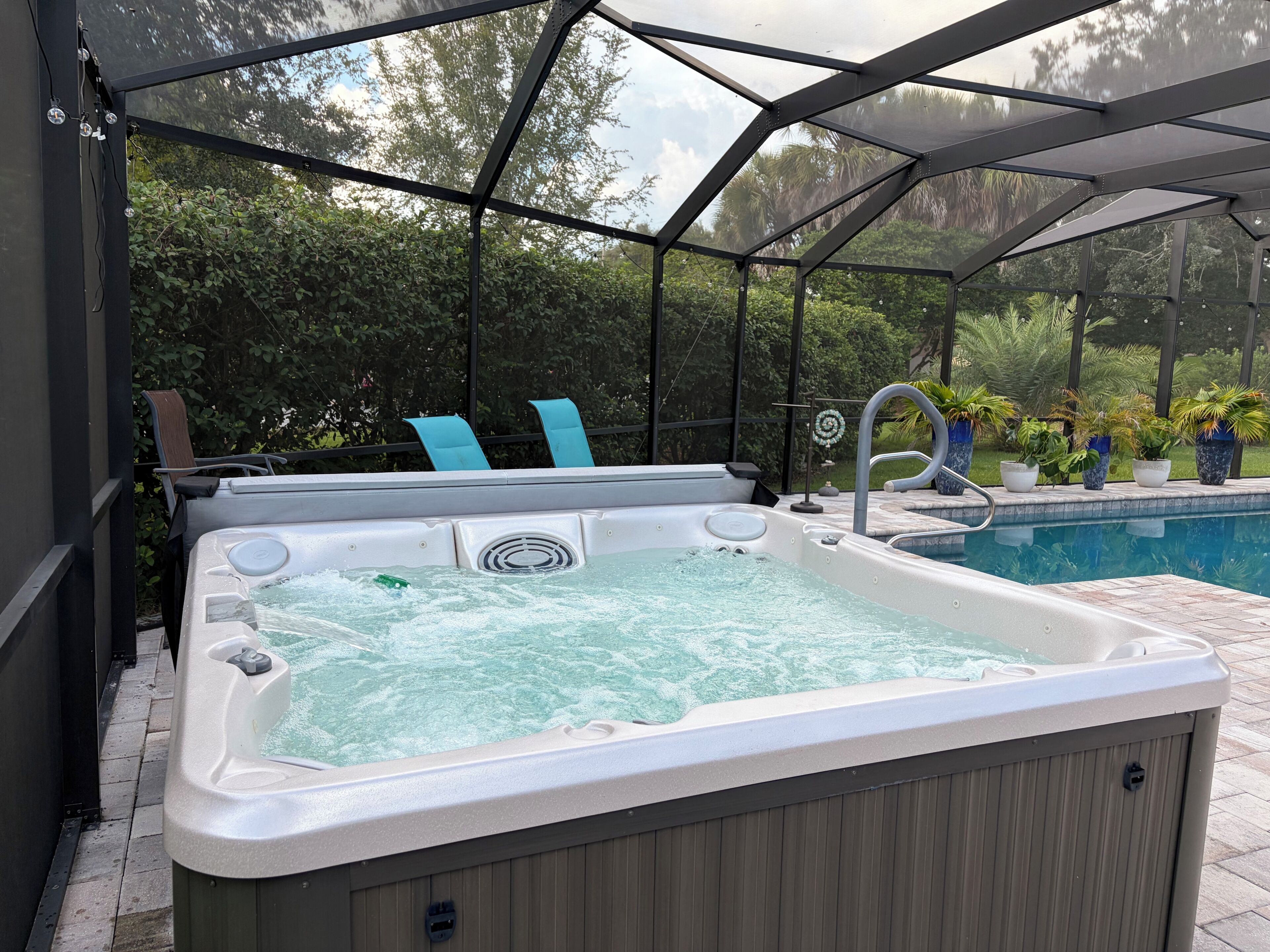 A hot tub with a cover, surrounded by a pool and potted plants.