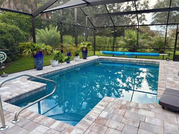 A covered outdoor swimming pool with a glass edge, surrounded by potted plants and a patio area.