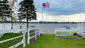 Una proprietà sul lungolago con un recinto bianco, un'asta con la bandiera americana e vista su un lago.