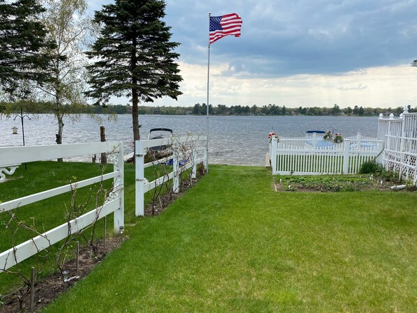 A waterfront property with a white fence, a flagpole with an American flag, and a view of a lake.