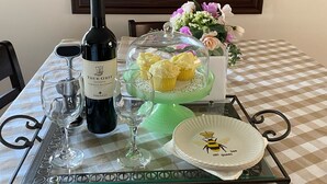Un tavolo da pranzo con tovaglia a quadri, una bottiglia di vino, bicchieri, un piatto con un motivo a ape e un vassoio per cupcake con dei cupcake.