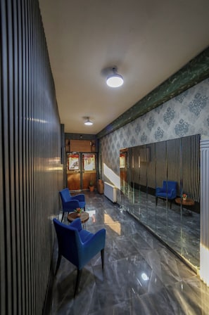 Un interior moderno con suelo de mármol, sillas azules, mostrador de recepción de madera y papel tapiz estampado.