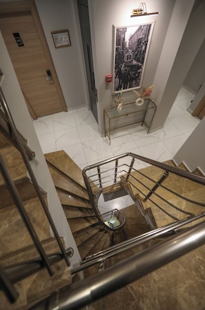 Una escalera con barandilla, una puerta de madera, un cuadro en la pared y una pequeña mesa con un florero.