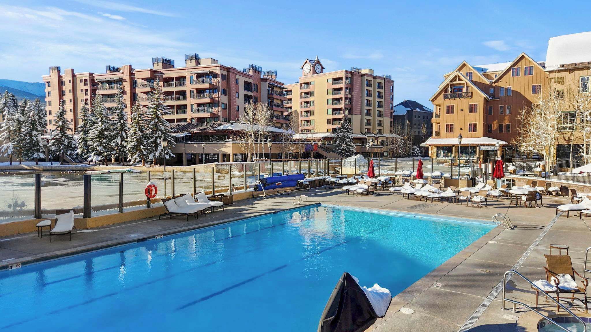 Una piscina con sillas de descanso y sombrillas, rodeada de edificios de varios pisos con balcones.