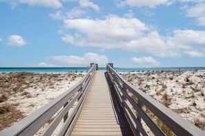 Een houten looppad dat naar een strand leidt, onder een heldere lucht.