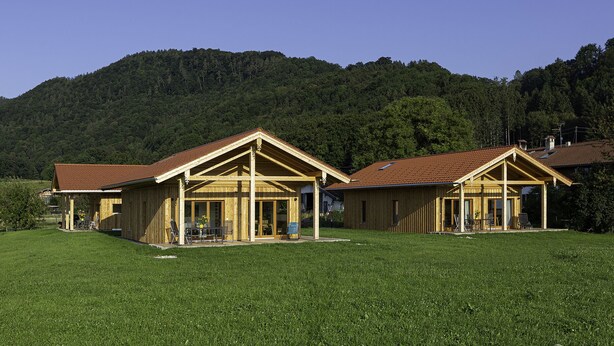 A wooden cabin with a sloped roof, a covered porch, and a view of a forested mountain.