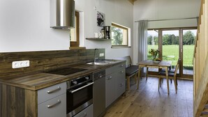 A modern kitchen with a wooden countertop, stainless steel appliances, and a view of a grassy area through a large window.