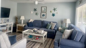Un salon avec un canapé bleu, une table basse blanche et un ventilateur de plafond.