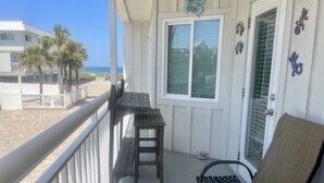 Un balcon avec vue sur la plage, un banc en bois, une chaise et une pancarte indiquant l'heure du « happy hour ».