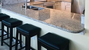 Une cuisine moderne avec des armoires blanches, un comptoir en granit, un réfrigérateur en acier inoxydable et une décoration en forme d’étoile de mer sur le mur.