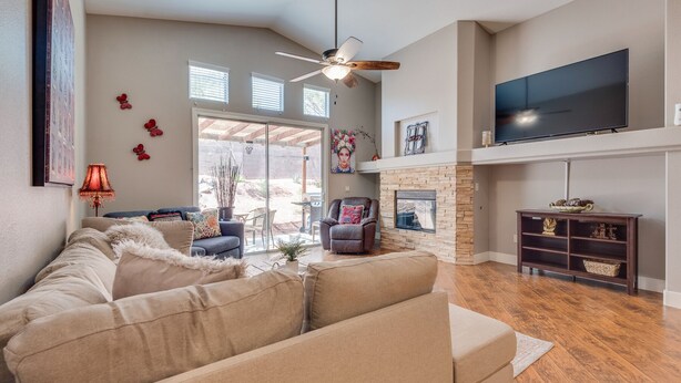 A spacious living room with a large sectional sofa, a fireplace, a flat-screen TV mounted above the fireplace, and a ceiling fan.