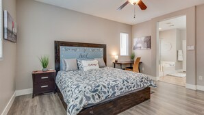 A bedroom with a wooden bed frame, a ceiling fan, a bedside table with a lamp, and a nightstand.