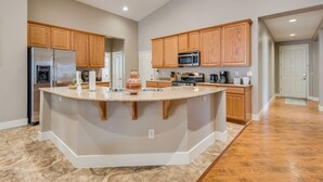 A spacious kitchen with a central island, wooden cabinets, stainless steel appliances, and a marble countertop.