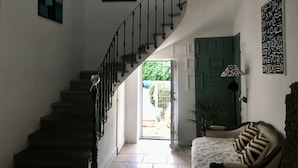 A staircase with a black railing leading to a door. There is a white fluffy rug and a patterned cushion on a wooden bench.