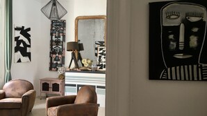 A living room with two brown armchairs, a geometric abstract painting, a large mirror, and a black and white abstract painting.