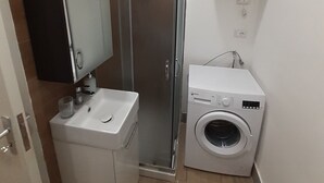 A compact bathroom with a sink, mirror, towel rack, shower, and a washing machine. - Piazza Roma holidays House  (Catania)