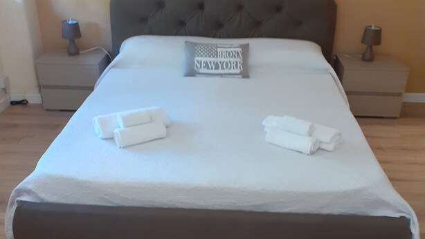 A neatly made bed with a pillow labeled "Bronx New York" and two rolled towels. - Piazza Roma holidays House  (Catania)