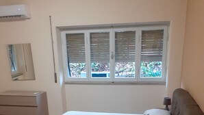 A bedroom with a bed, a dresser, a window with blinds, and an air conditioning unit. - Piazza Roma holidays House  (Catania)